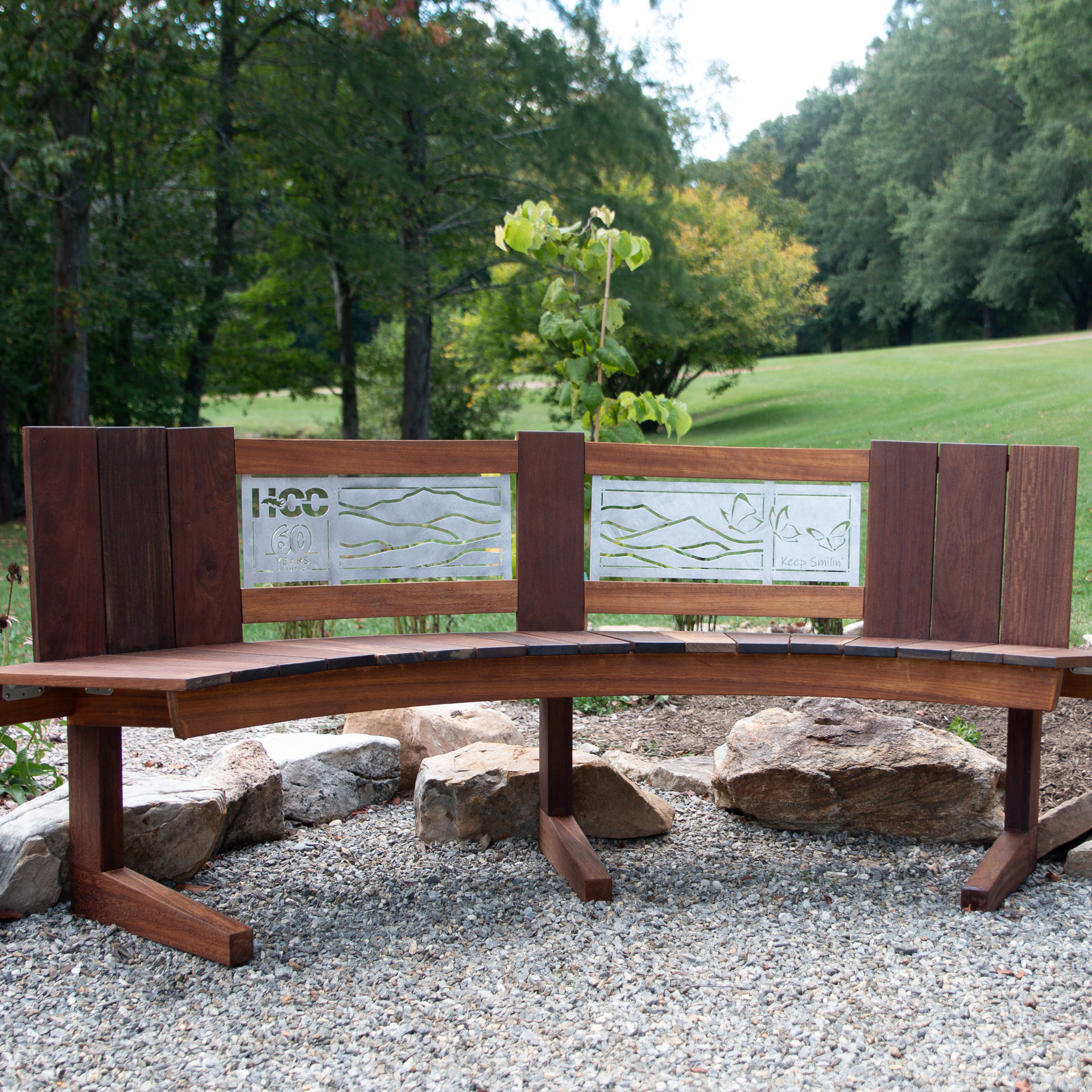 wood bench with metal inlay in gravel area in front of grass and trees